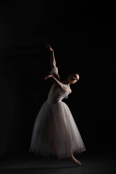 Professional ballerina dancing ballet.Ballerina in a white dress and pointe shoes. Dark background. Beautiful female body. - Fotoğraf, Görsel