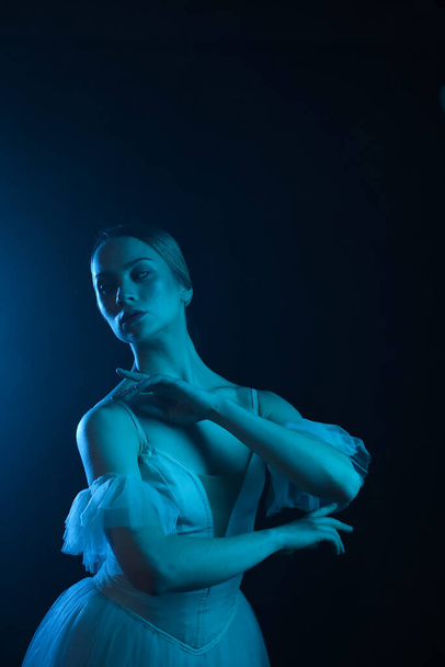 Professional ballerina dancing ballet.Ballerina in a white dress and pointe shoes. Dark background, blue light. Veil. Scene. Performance - Фото, изображение