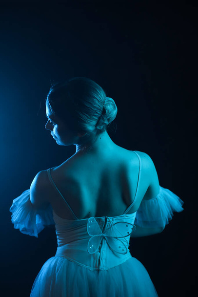 Professionelle Ballerina tanzt Ballett. Ballerina in einem weißen Kleid und Spitzenschuhen. Dunkler Hintergrund, blaues Licht. Schleier. Szene. Leistung - Foto, Bild