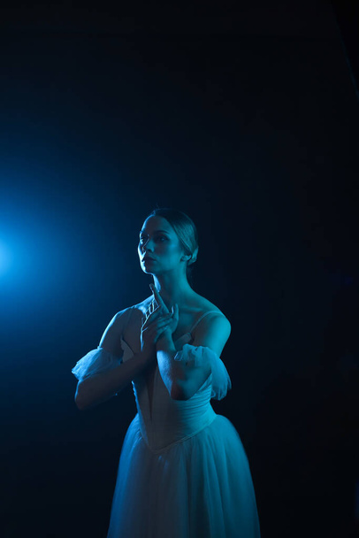 Professionelle Ballerina tanzt Ballett. Ballerina in einem weißen Kleid und Spitzenschuhen. Dunkler Hintergrund, blaues Licht. Schleier. Szene. Leistung - Foto, Bild