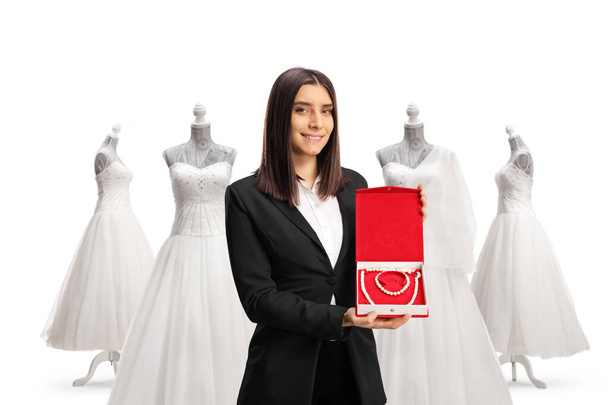 Young woman holding a box with a pearl necklace and bracelet in front of bridal gowns isolated on white background - Foto, imagen