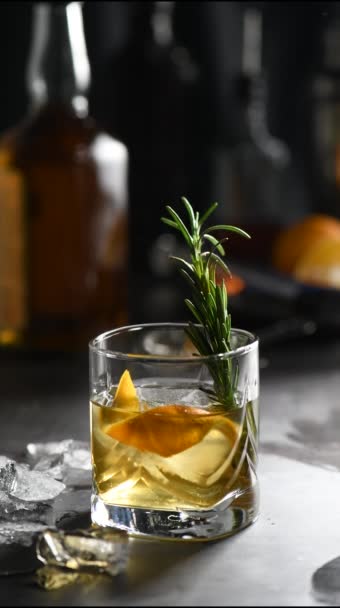 Cocktail Old Fashioned Negroni. Die Adstringenz des Whiskys wird durch Zucker ausgeglichen, und die Kräutertinktur und der Räucherrosmarin verleihen dem Whisky Geschmack und originelle Noten. Serviert mit Eis und Orange - Filmmaterial, Video