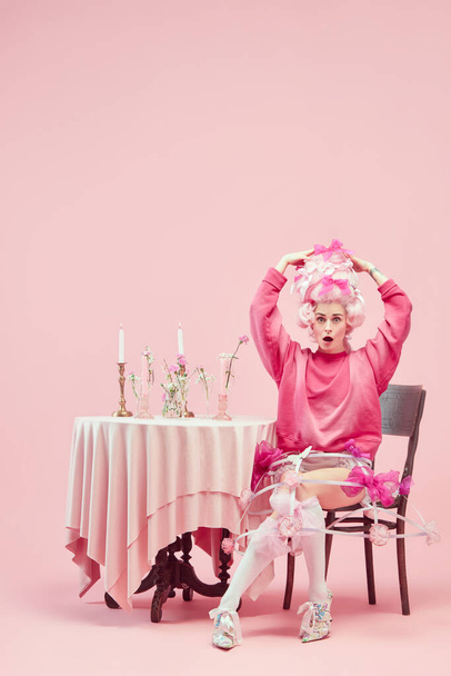 Nieuw kapsel. Portret met vrouw, prinses in chique roze kleren kijkend naar camera met geschokt gezicht op roze achtergrond. Concept van vergelijking van tijdperken, moderniteit en renaissance, schoonheid, geschiedenis - Foto, afbeelding