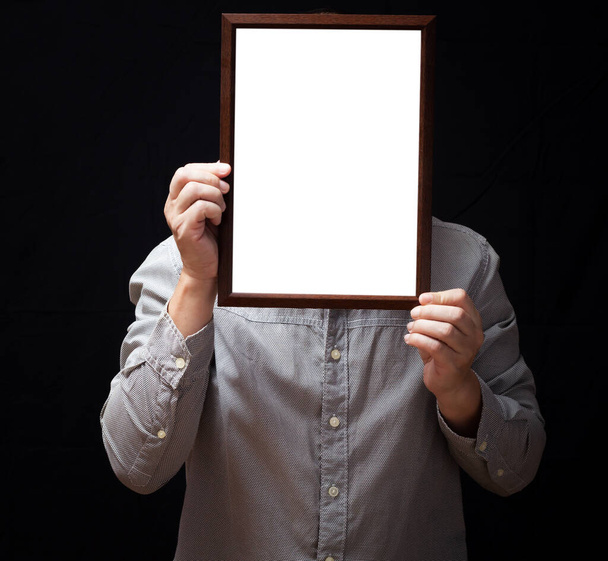 A blank diploma or a mockup certificate in the hand of a man employee wearing shirt on black background. The vertical picture frame is empty and the copy space. - Photo, image