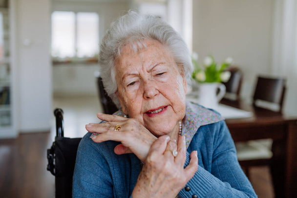 Portrait of senior woman on wheelchair with pain in her arm. - Фото, изображение