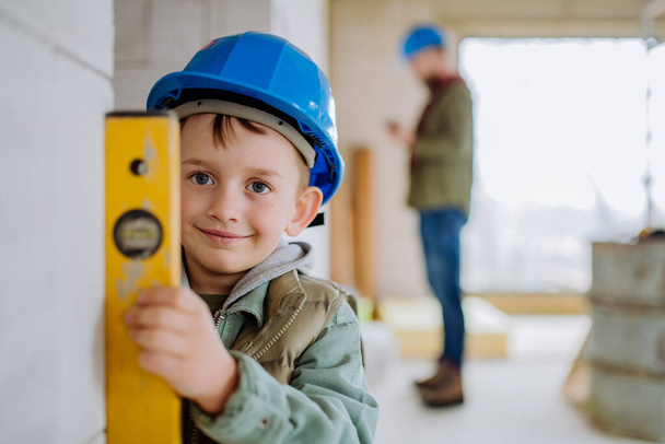 Little boy in unfinished house measuring wall in unfinished house with a spirit level. - Foto, imagen