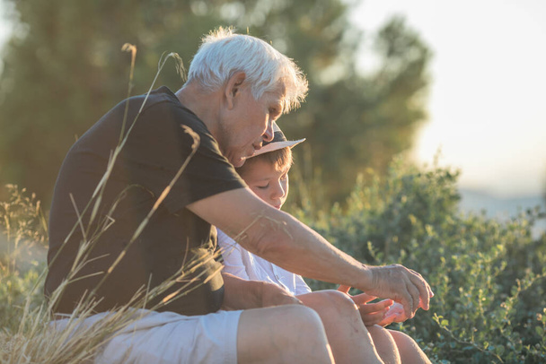 Nagyapa és unokája élvezik a szabadban, mosolyogva és ölelkezve. A barátságos család fogalma. - Fotó, kép
