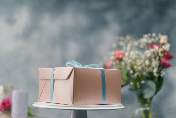 a packed delicious cake in a gift box with a bow stands on stand on a background of flowers - Photo, Image