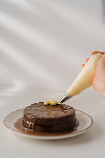 délicieux gâteau au chocolat fraîchement fait Sacher ou Prague sur un fond blanc décoré avec de la crème à partir de manches de pâtisserie - Photo, image