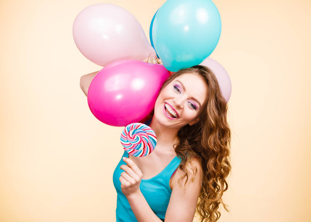 Woman attractive cheerful girl holding colorful balloons and sweet lollipop in hands. Summer holidays, celebration and happiness concept. Studio shot bright yellow background - Fotografie, Obrázek