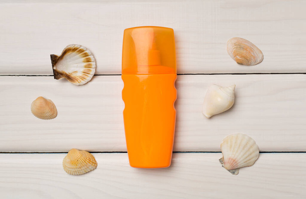 Bottle with sun protection cream and sea shells on wooden background, top view. - Fotó, kép