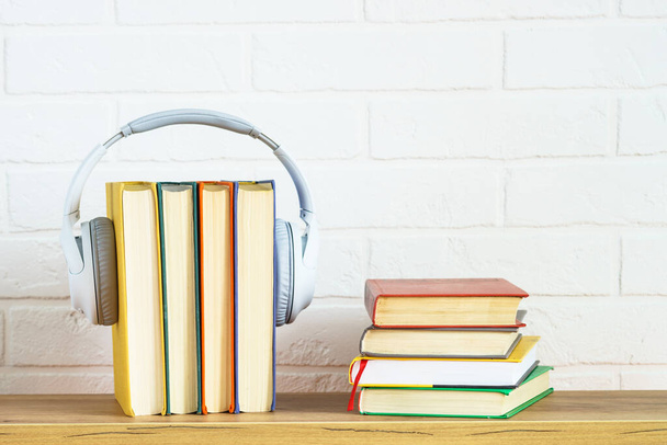 Ses kitapları konsepti. Kablosuz kulaklıklar ve ahşap masa beyaz arka planda renk kitapları. - Fotoğraf, Görsel