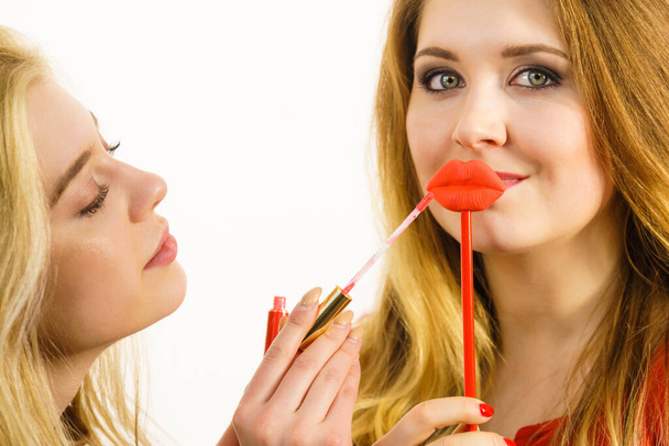 Young adult woman applying lipstick or lip gloss, getting her make up done holding fake lips on stick - Фото, зображення
