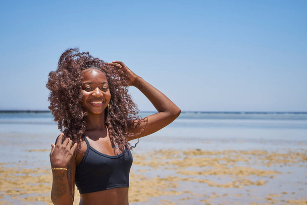 Young smiling brazilian woman on summer vacation standing at beach and enjoying sea breeze.Sexy bikini body woman feeling free on holidays.                             - Foto, Imagen