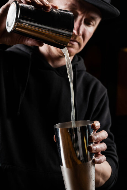 Bartender is pouring and mixing Penicillin cocktail at the bar. Bartender mixes whiskey, lemon juice, and honey-ginger syrup to prepare the Penicillin alcoholic cocktail - Photo, Image