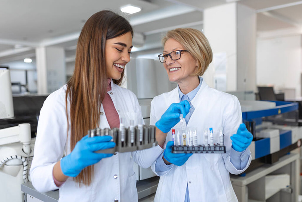 Два учёных работают в лаборатории. Молодая женщина-исследователь и ее старший руководитель проводят исследования с помощью пробирки
. - Фото, изображение