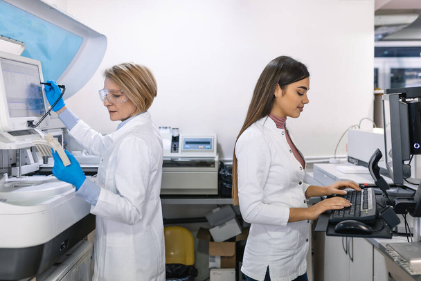 Ομάδα ερευνητών επιστημόνων που εργάζονται στον υπολογιστή, με ιατρικό εξοπλισμό, αναλύοντας δείγματα αίματος και γενετικού υλικού με ειδικές μηχανές στο σύγχρονο εργαστήριο. - Φωτογραφία, εικόνα