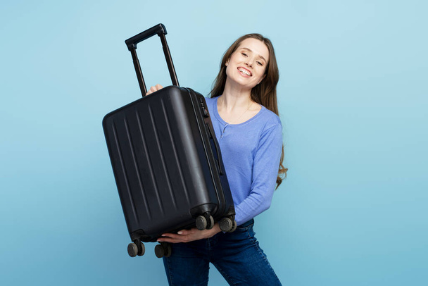 Giovane donna sorridente, viaggiatore che tiene la valigia pronta per le vacanze, isolata su sfondo blu. Concetto di viaggio - Foto, immagini