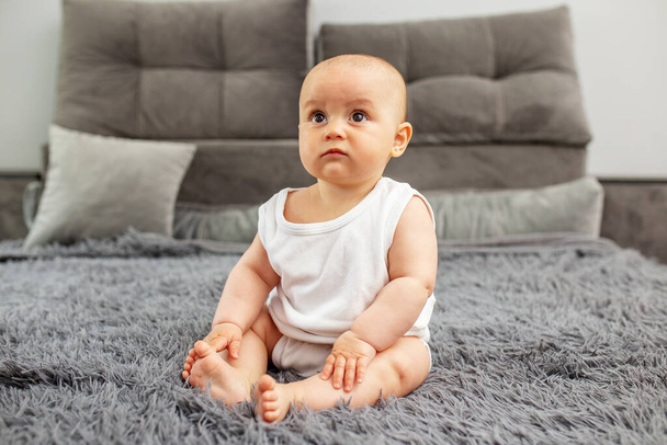Little baby boy or girl sitting on bed at home. Childhood, babyhood and care concept. Baby development. - Fotó, kép