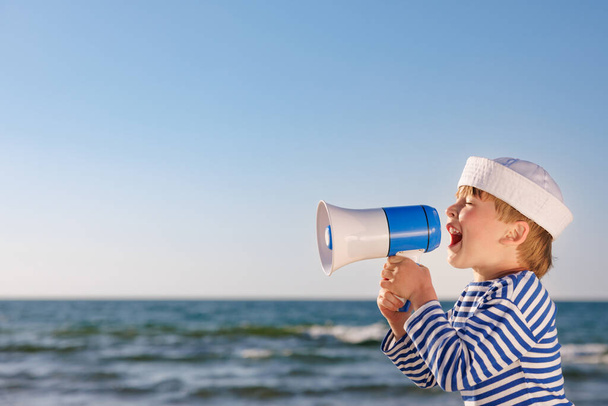 Happy child pretend to be sailor. Kid agains blue sea and sky. Boy on summer vacation. Child shouting through loudspeaker. Adventure and travel concept - Foto, imagen