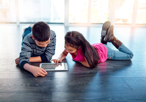Ils sont toujours télécharger de nouveaux jeux sur Internet. deux jeunes enfants qui utilisent une tablette numérique alors qu'ils sont couchés sur le sol à la maison - Photo, image