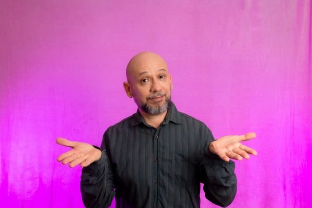 Portrait of serious man, 50 years old, with beard and bald head making hand signals. Isolated on pink background. - 写真・画像