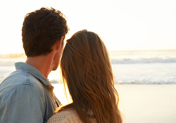 Romance verdadeiro. Um jovem casal abraçando um ao outro e observando o pôr do sol na praia - Foto, Imagem