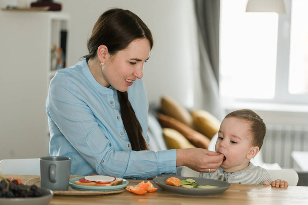 Young mother feeding her baby son with fruit puree - Foto, afbeelding