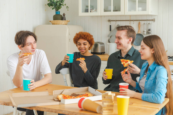 Домашняя вечеринка. Друзья проводят время вместе, веселясь, общаясь дома. Счастливые разнообразные группы едят пиццу пить пиво или лимонад. Лучшие друзья смешанной расы наслаждаются выходными - Фото, изображение