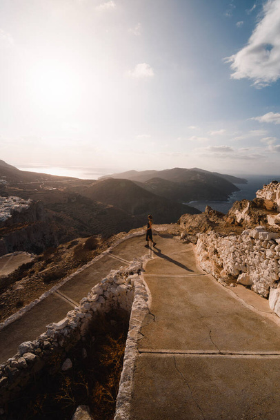 young woman walking down a path at sunset on greek island of Folegandros with the sea in the background - Fotoğraf, Görsel