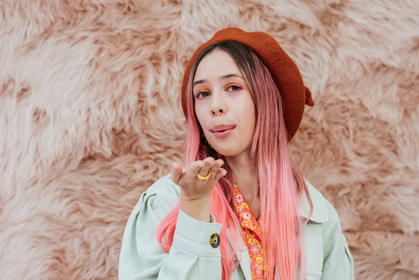 Stylish millennial teenager girl with color hair sends an air kiss. Portrait of a romantic young woman in a beret on a pink background. - Photo, Image