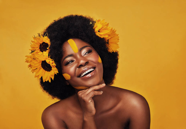 The face of natural beauty. Studio shot of a beautiful young woman smiling while posing with sunflowers in her hair against a mustard background - Fotoğraf, Görsel