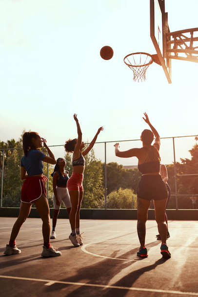 Schoot en scoort ze. een diverse groep sportvrouwen die overdag samen een competitief basketbalspel spelen - Foto, afbeelding