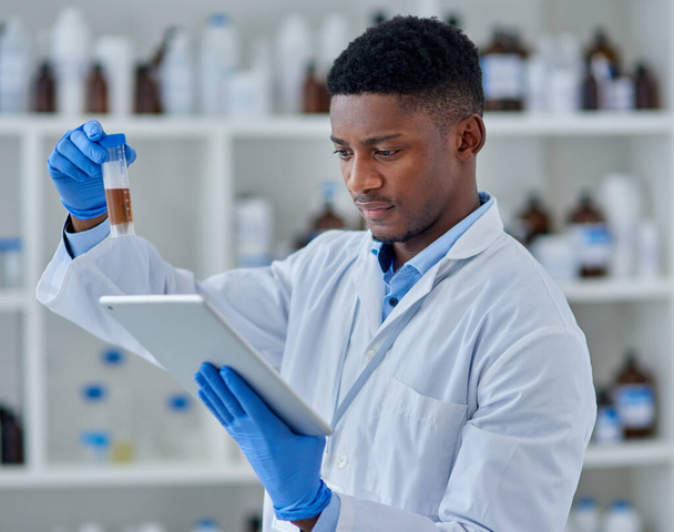 This is very peculiar. a focused young male scientist working on a digital tablet while studying a vial with a substance inside of it at a laboratory - Photo, Image