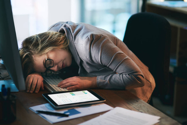 Solo una siesta rápida es todo lo que necesito... una joven mujer de negocios durmiendo en su escritorio en una oficina por la noche - Foto, imagen