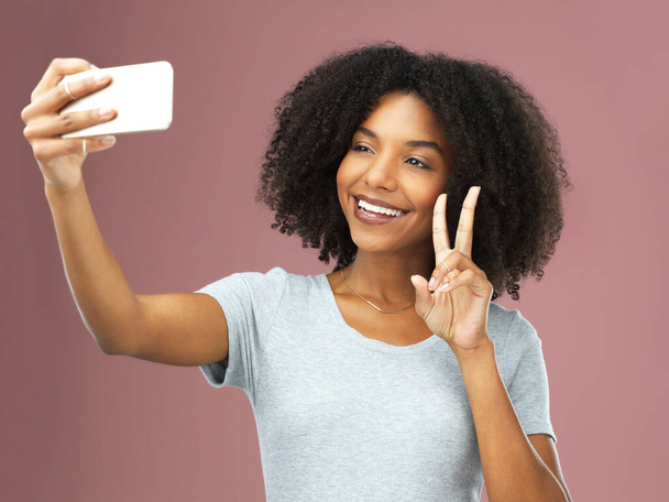 Maar eerst een selfie. Studio shot van een aantrekkelijke jonge vrouw het nemen van een selfie tegen een roze achtergrond - Foto, afbeelding