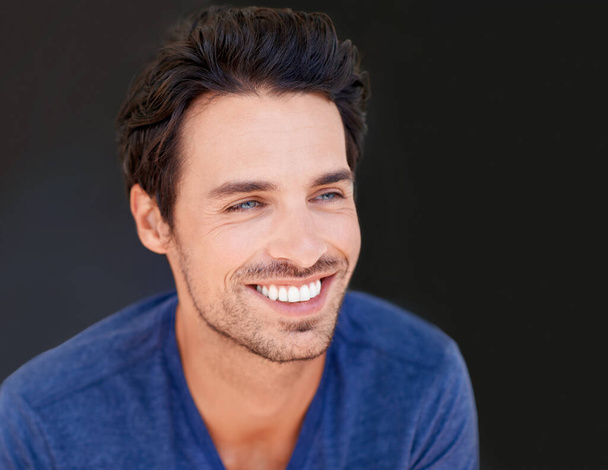 Face, smile and handsome man or happy male with white teeth or oral hygiene and isolated on a dark, black background. Motivated, cheerful and attractive guy or dental health or beauty in studio. - Photo, Image