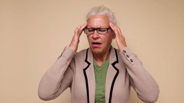Пожилая европейка страдает от головной боли и прижимает пальцы к вискам - Фото, изображение