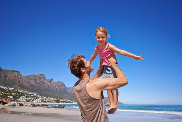 Моменты отца и дочери. Отец, играющий со своей маленькой дочерью на пляже в лучах солнца - Фото, изображение