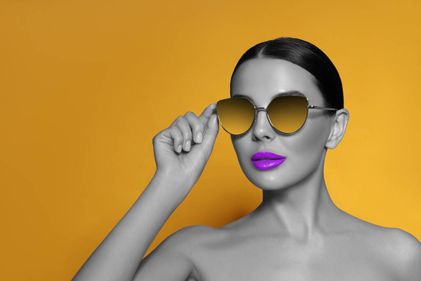 Attraktive Frau mit stylischer Sonnenbrille auf orangefarbenem Hintergrund. Farbakzent - Foto, Bild