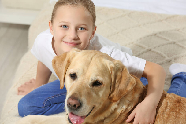 Cute child with her Labrador Retriever on bed. Adorable pet - Photo, Image