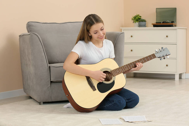 Teenage girl playing acoustic guitar in room - Foto, afbeelding