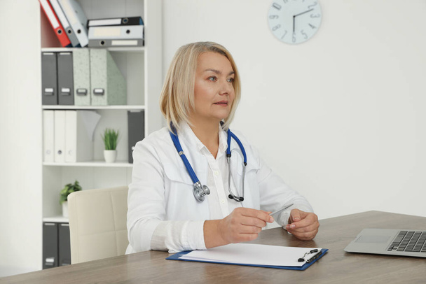 Doctor sitting at wooden table in clinic - Φωτογραφία, εικόνα