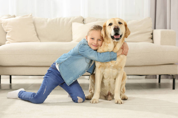 Cute child hugging her Labrador Retriever on floor at home. Adorable pet - Foto, afbeelding