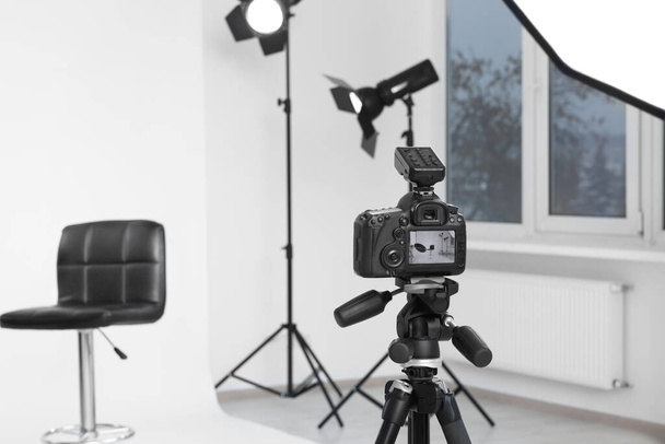 Camera on tripod, bar stool and professional lighting equipment in modern photo studio, space for text - Fotoğraf, Görsel