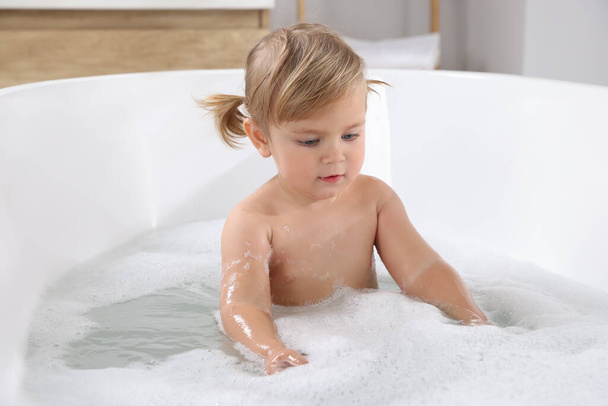 Cute little girl taking foamy bath at home - Фото, изображение