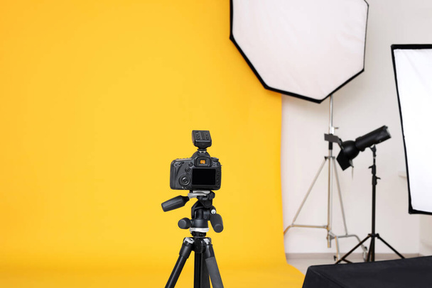 Camera on tripod and professional lighting equipment in modern photo studio - Фото, изображение
