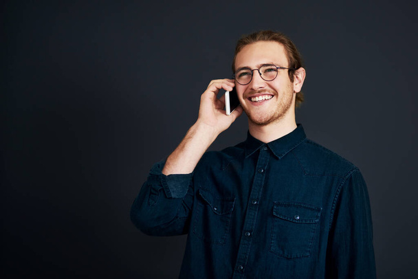Sealing the deal over the phone. a handsome young businessman standing and talking on his cellphone against a black background in the studio - Foto, Imagen