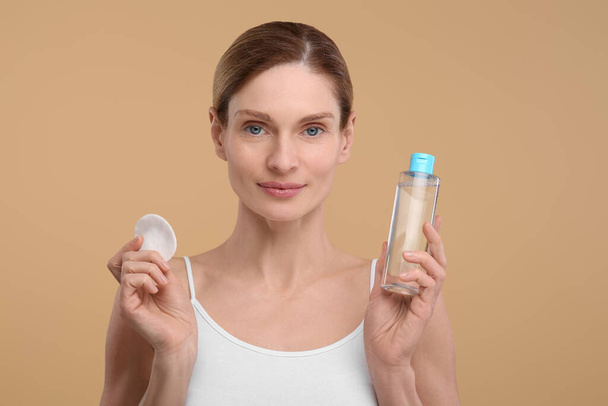 Beautiful woman with makeup remover and cotton pad on beige background - Φωτογραφία, εικόνα
