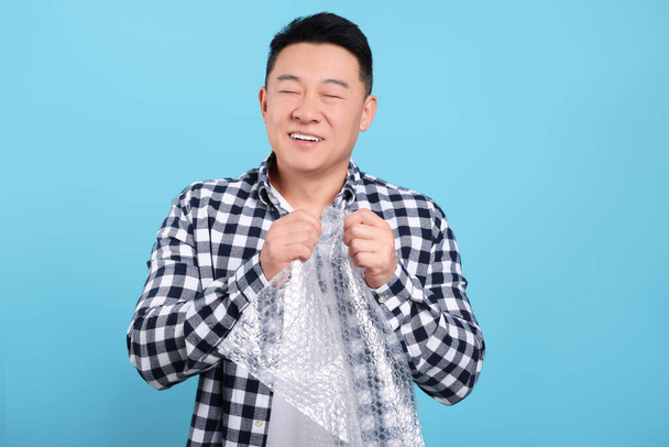 Happy asian man with bubble wrap on light blue background - Photo, image